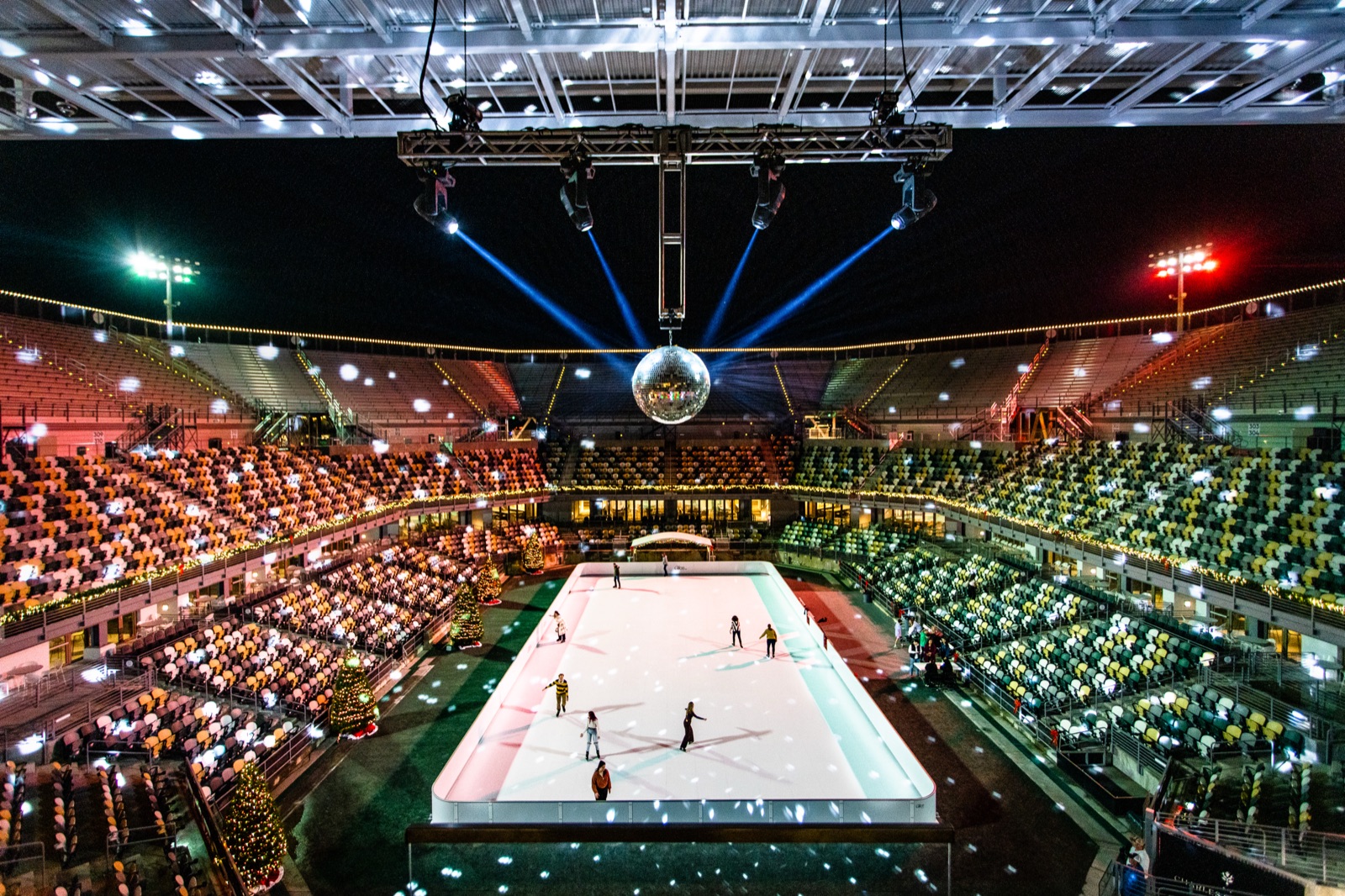 The full seating bowl of Credit One Stadium in Charleston seen from above at night, with a small Glice rink lit in the middle of the arena floor and skaters on it