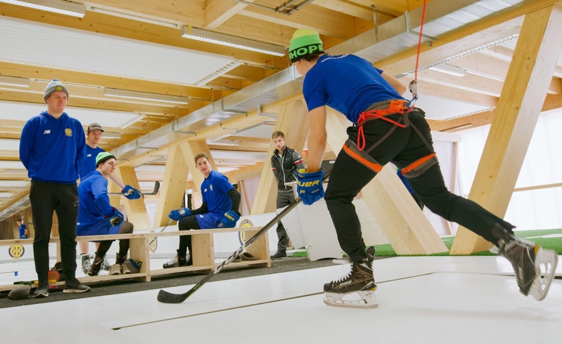 Hockey player skating on a Glice Skatemill while secured by a safety harness