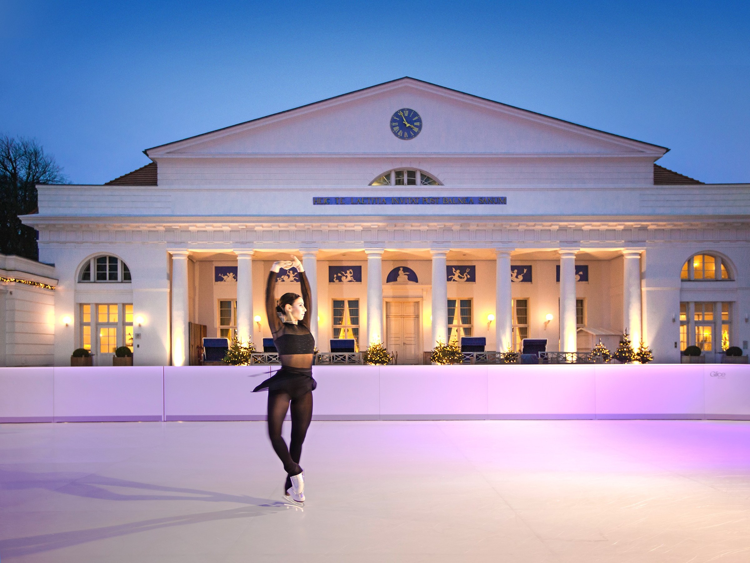 Łyżwiarka figurowa na lodowisku Glice przed oświetlonym Grand Hotel Heiligendamm