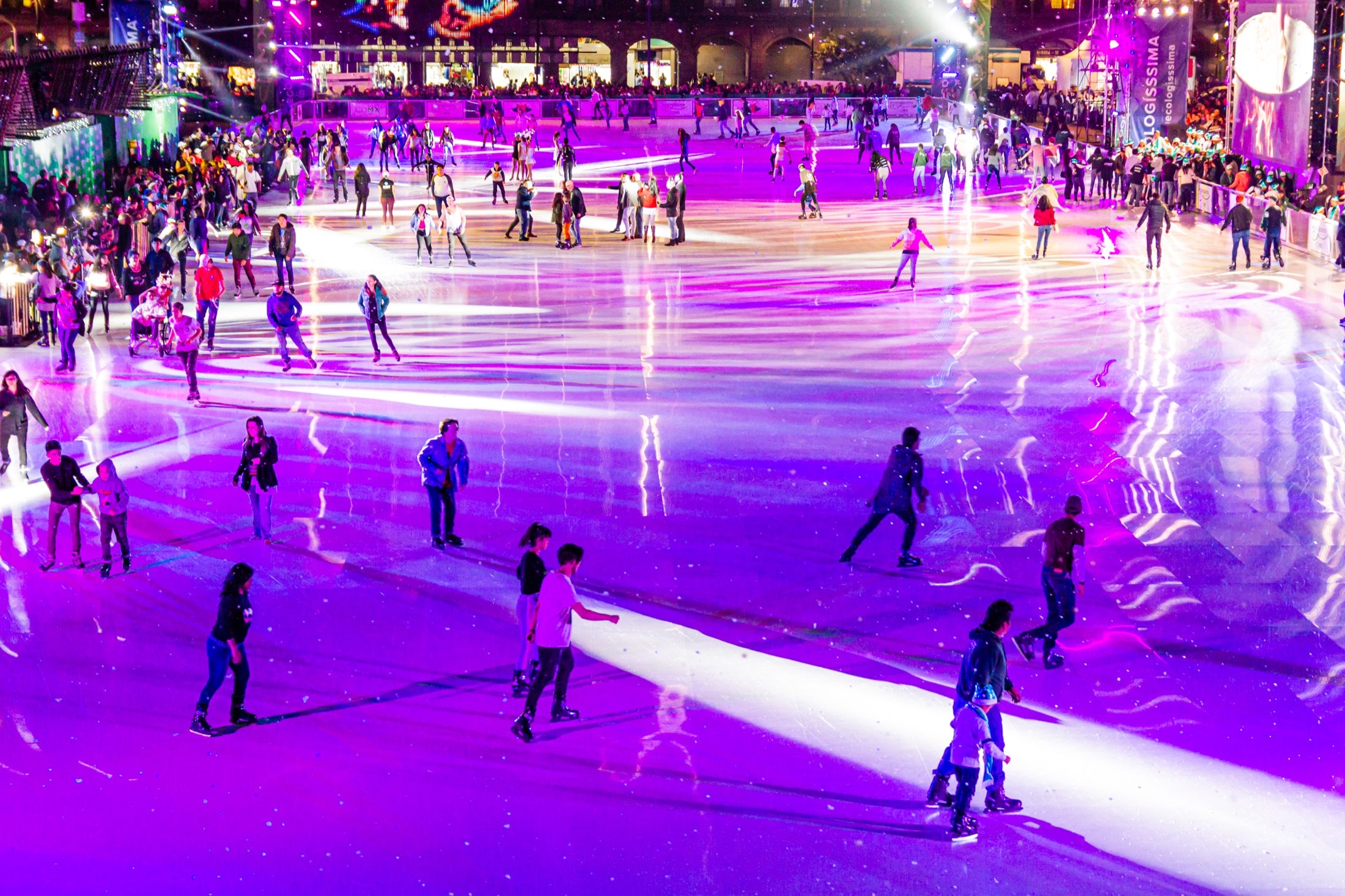 Elevated view of a large rink filled with skaters under purple event lighting