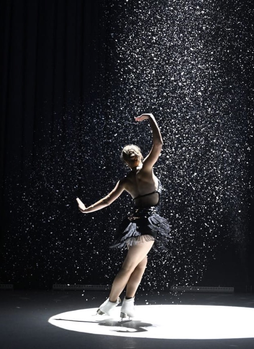 A figure skater performing under a spotlight on a Glice synthetic ice surface