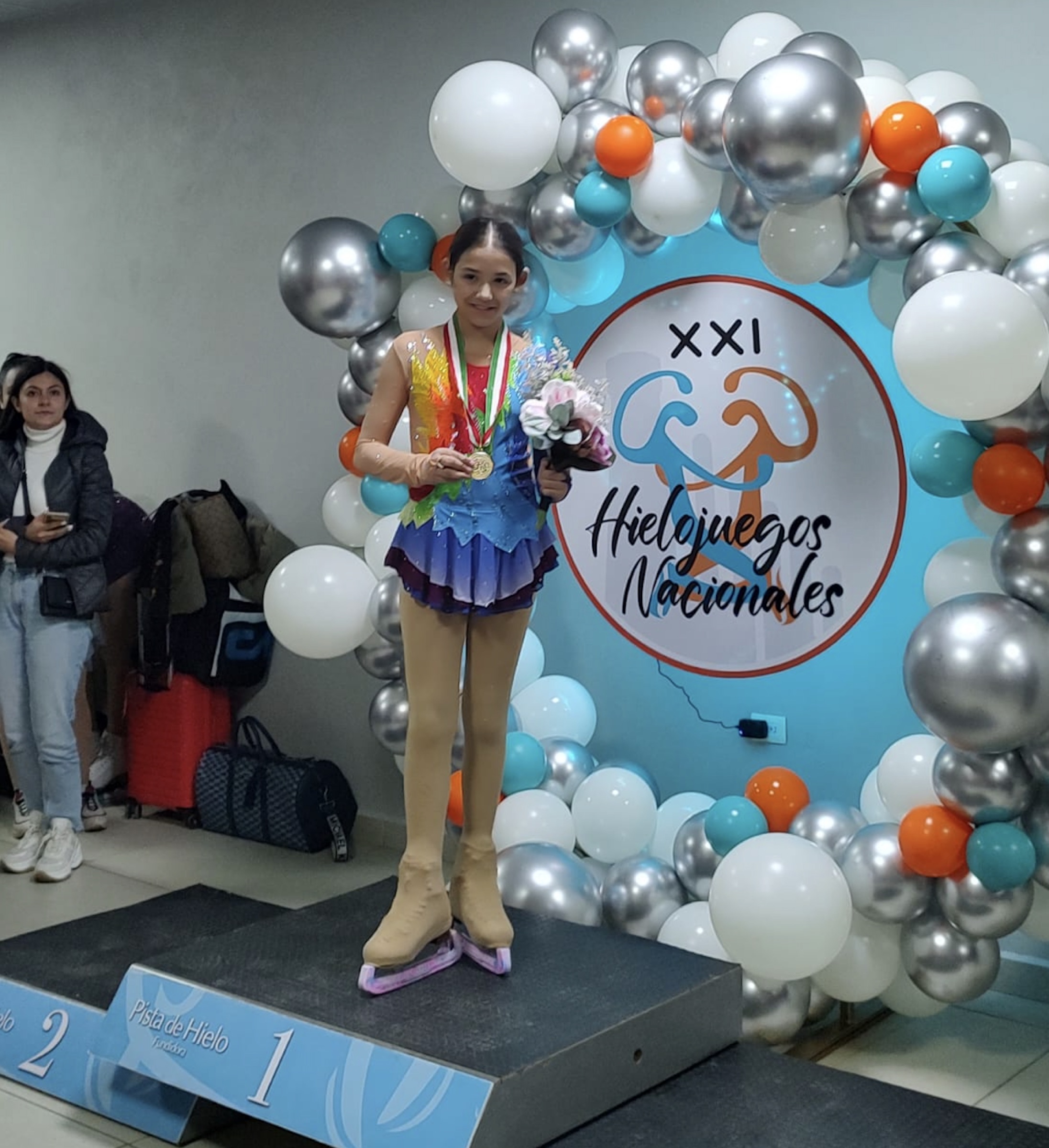 A skater who trained on Glice standing on the top step of the podium with a gold medal at a competition held on refrigerated ice