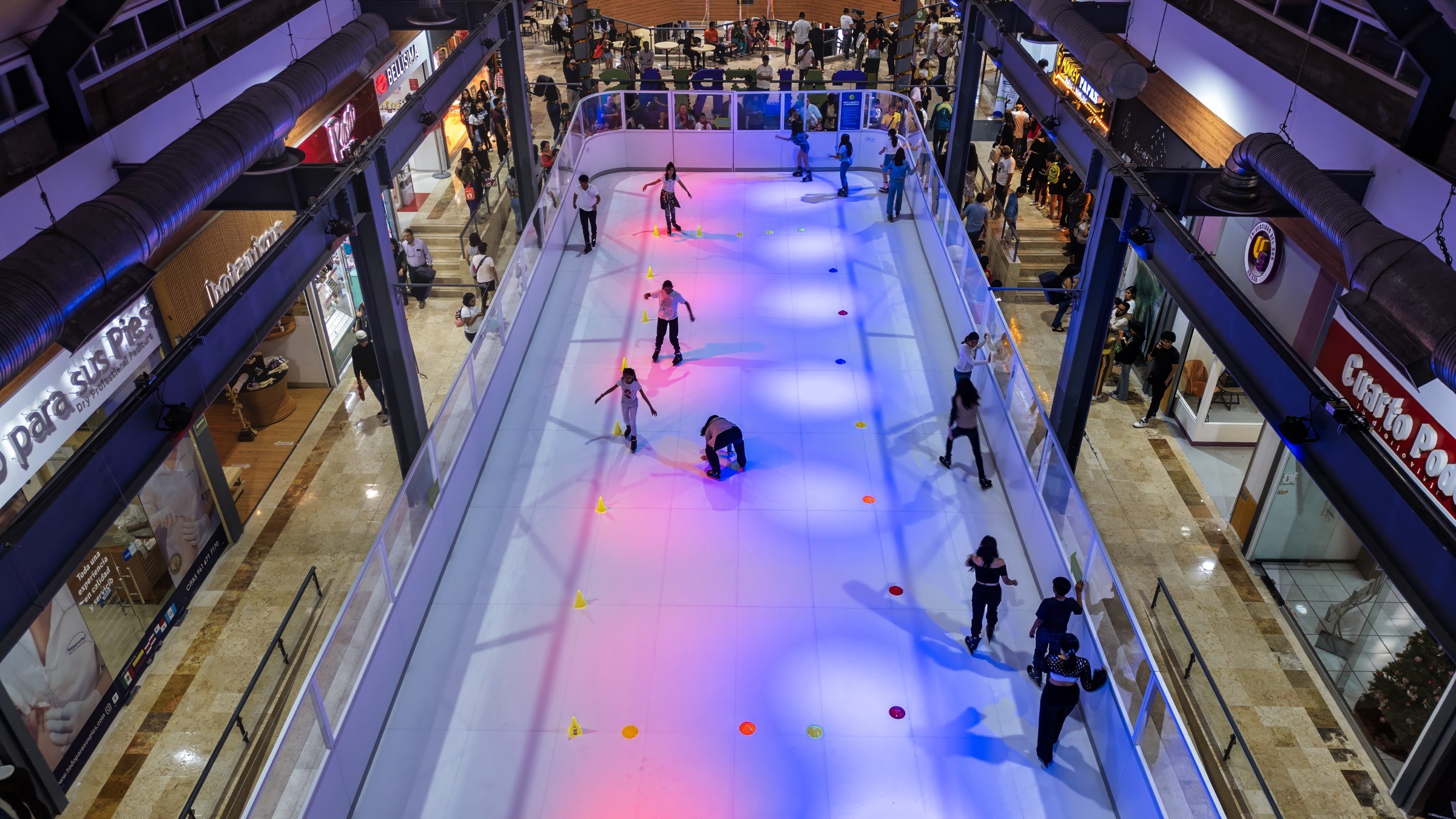 Overhead view of visitors skating on a colorful illuminated rink inside a shopping mall in Chiapas