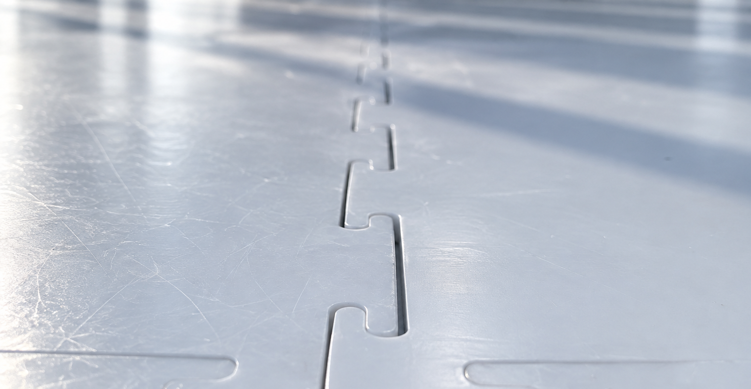 Close-up of a synthetic ice panel joint where one panel edge has bowed above the neighbouring surface