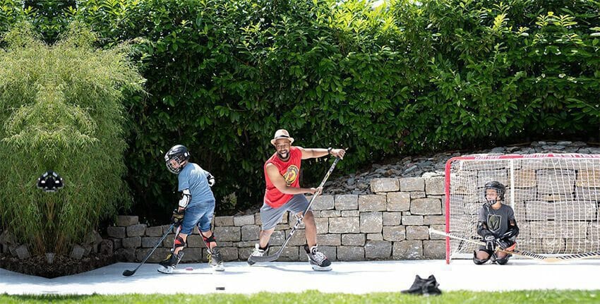 Father and two boys practicing hockey on backyard synthetic ice rink