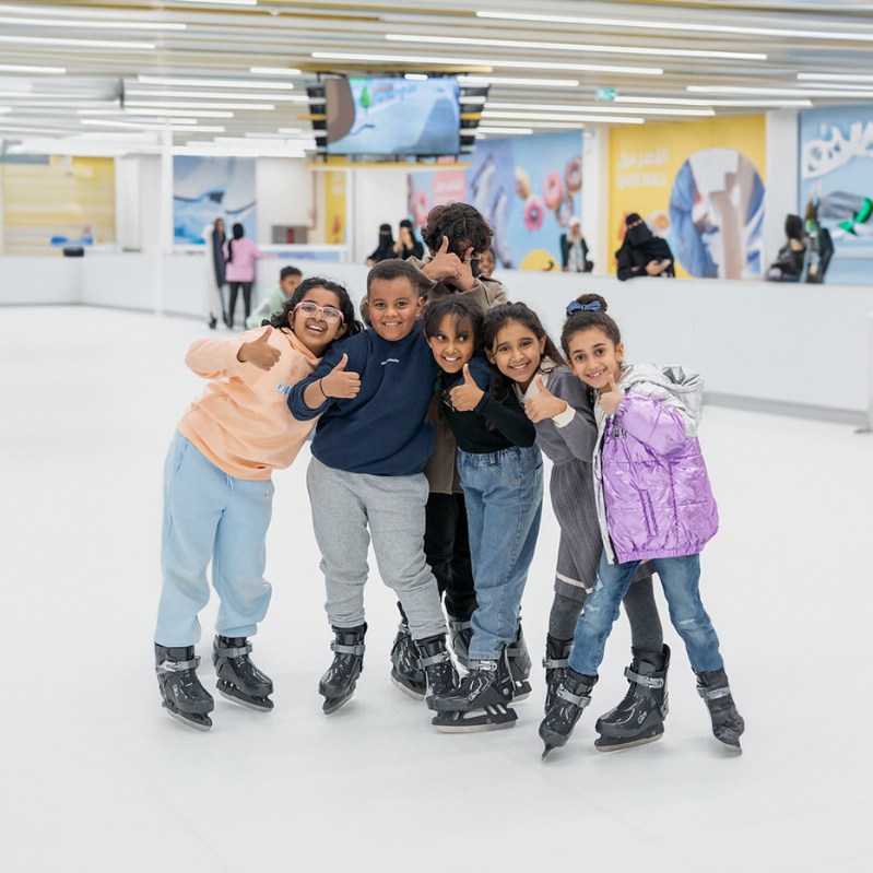 kids holding their thumbs up while standing on ice rink
