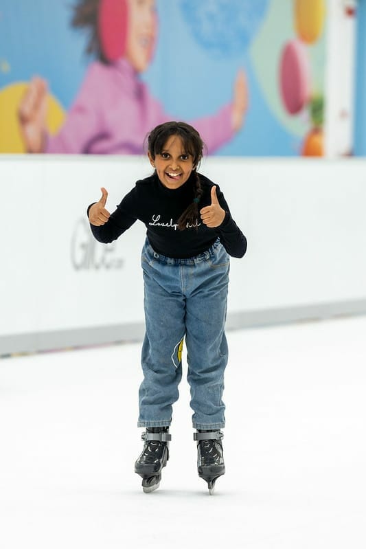 Girl showing thumbs up while ice skating