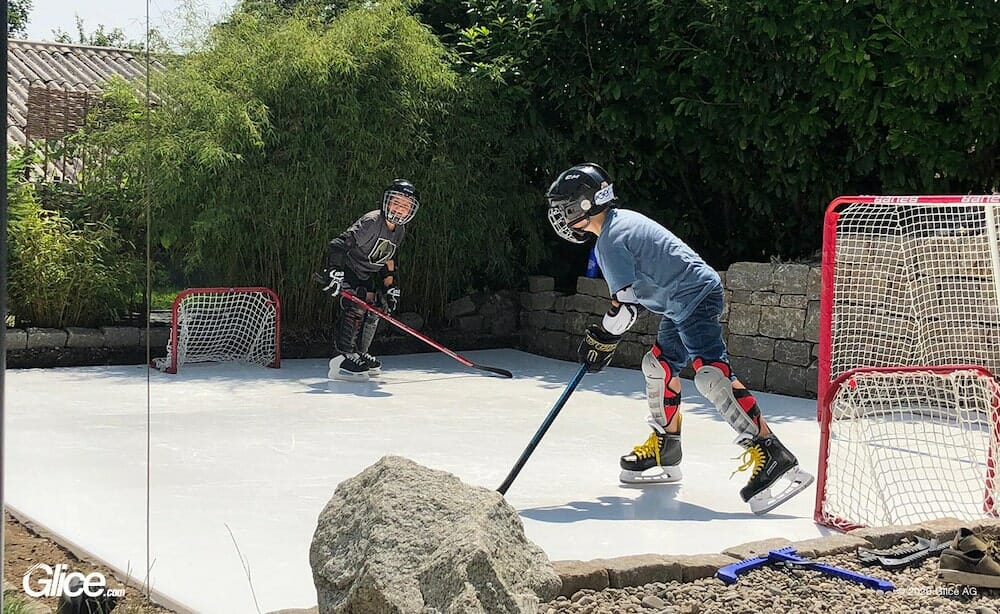 Two boys playing ice hockey on a synthetic ice rink in their backyard