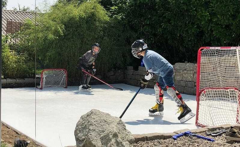 Two boys playing ice hockey on backyard ice rink